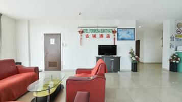 Un vestíbulo de hotel con asientos rojos, una mesa de vidrio, un televisor y un letrero en un idioma extranjero.