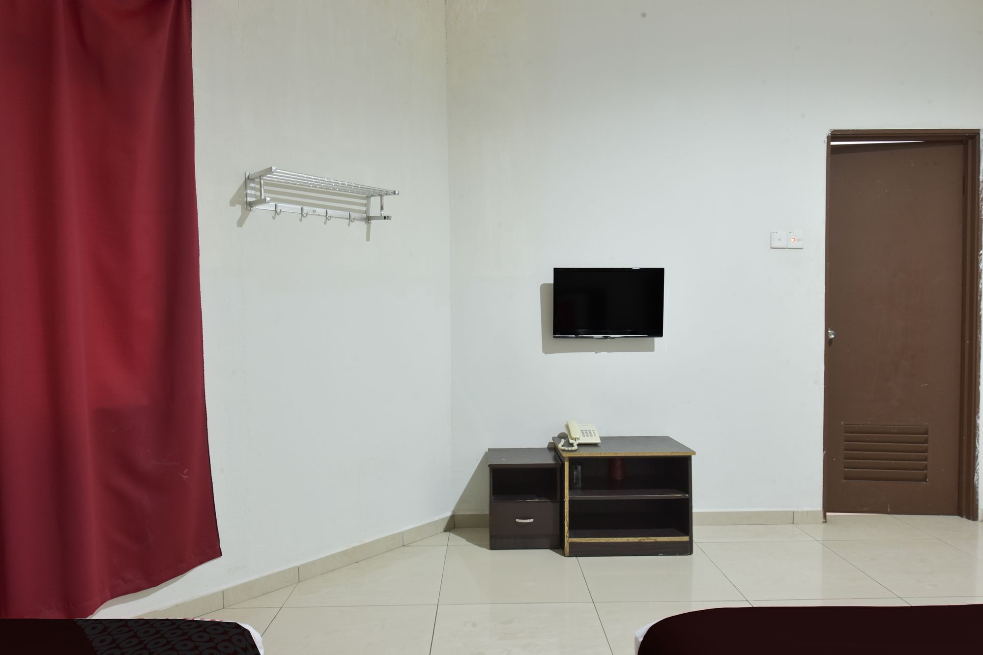 A room with a TV mounted on the wall, a small desk with a telephone, a red curtain, and a door.