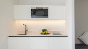 A compact kitchenette with a built-in oven, a sink, and a countertop with a bowl of fruit. - Akrogiali Garden Hotel (Hersonissos)