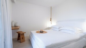 A white bedroom with a bed, a small wooden stool, and two vases on a shelf. - Akrogiali Garden Hotel (Hersonissos)