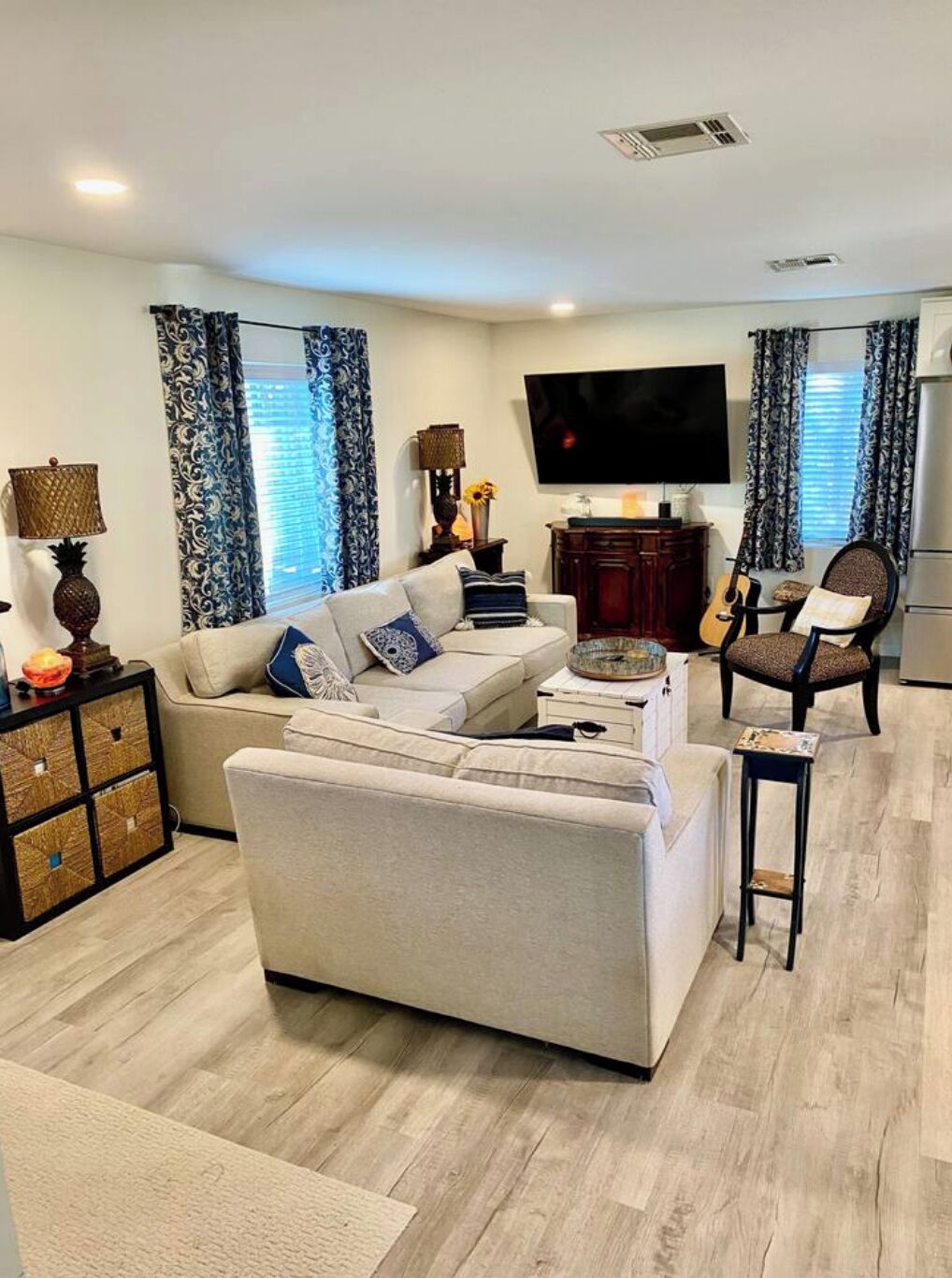 A modern living room with a sofa, armchairs, a TV, and a guitar.