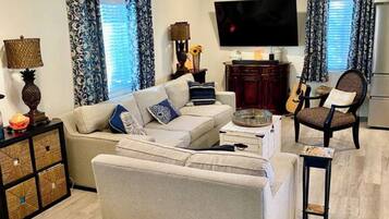 A modern living room with a sofa, armchairs, a TV, and a guitar.