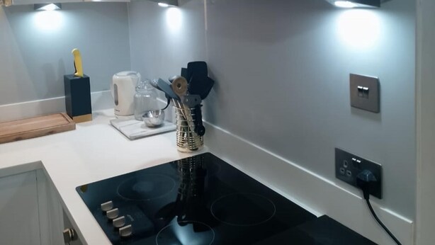 Une cuisine moderne dotée d’une plaque de cuisson à induction noire, d’une bouilloire, d’une machine à café et d’un porte-ustensiles sur le plan de travail.