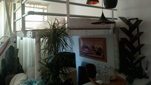 Une pièce avec une échelle en métal blanche, une grande plante en pot, une table à manger avec des chaises et un tableau accroché au mur.