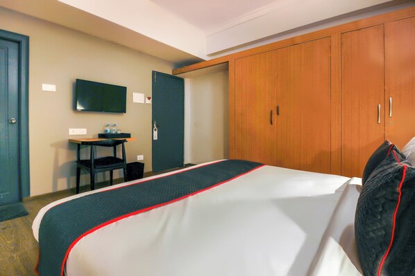 Habitación de hotel con cama, escritorio con silla, televisor y armario.