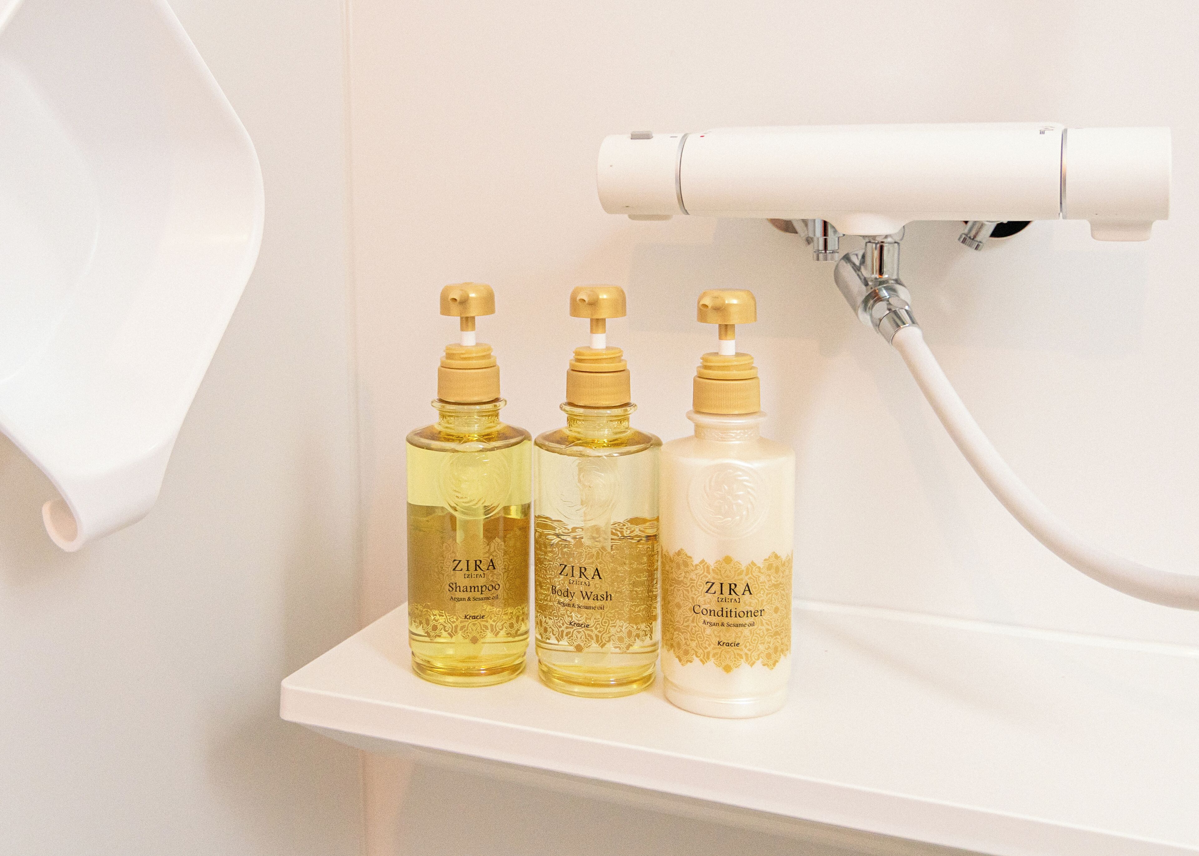 Drie flessen ZIRA body wash en conditioner op een witte plank in een badkamer.