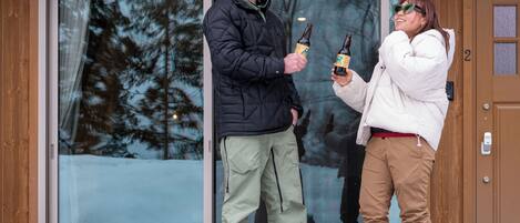 Two people standing in front of a wooden door with a glass window, holding beer bottles.