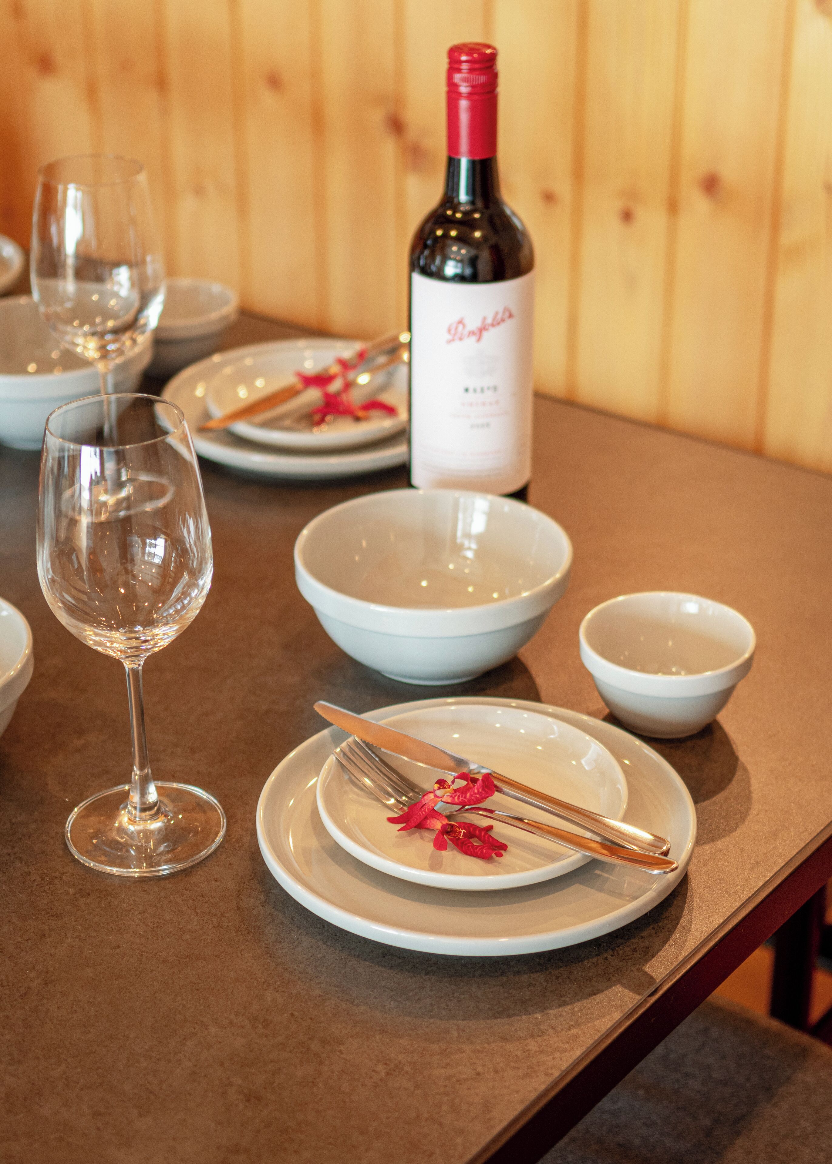 A dining table set with white plates, bowls, a wine bottle, and cutlery.