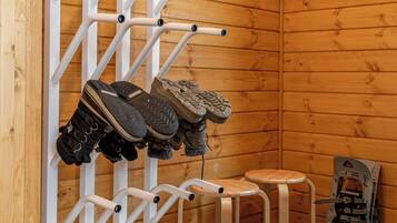 A wooden room with a shoe rack holding boots, a small stool, and a snowboard leaning against the wall.