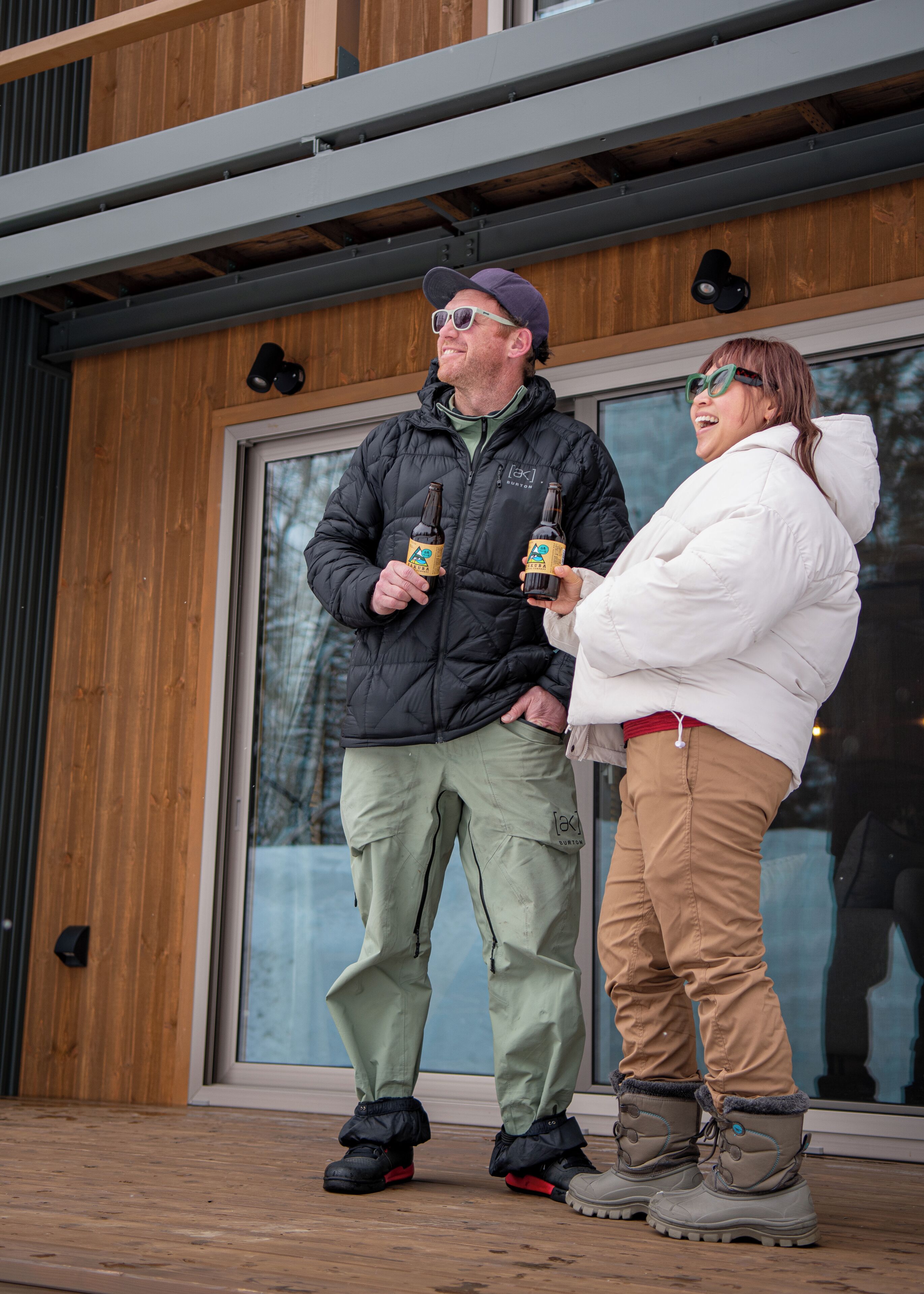 Two people standing outside a building with a wooden facade and large windows.