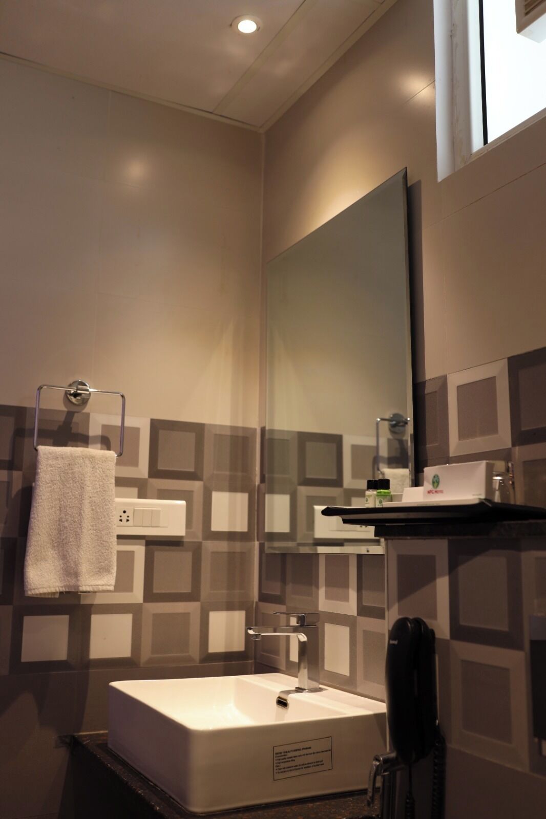 Un baño con un lavabo blanco, una toalla colgada en un perchero metálico, un espejo y un teléfono negro.