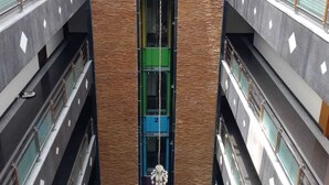A multi-level atrium with a central elevator shaft, glass railings, and a chandelier. - NPG Hotel (KA)