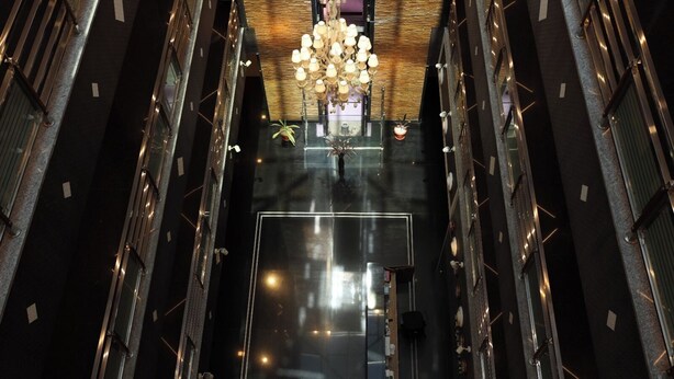 A high-ceilinged atrium with a central chandelier, reflective floor, and metal railings. - NPG Hotel (KA)