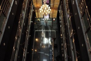 A high-ceilinged atrium with a central chandelier, reflective floor, and metal railings.