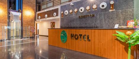 A hotel reception desk with a wooden finish, a green logo, and a reception sign.