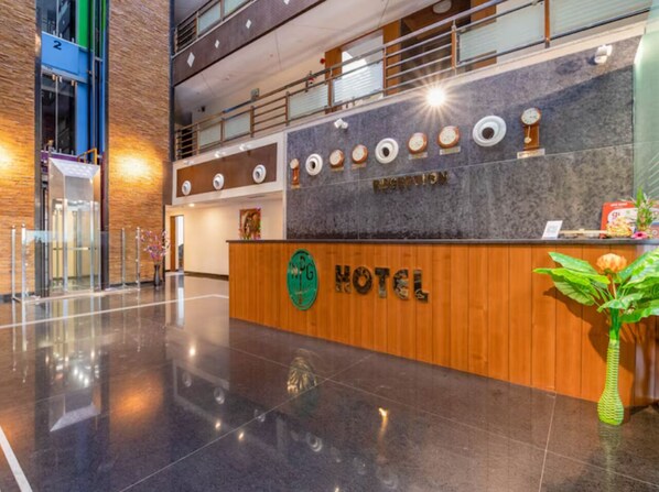 Un mostrador de recepción de hotel con detalles de madera, un logo verde y un cartel de recepción.