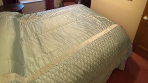 Un dormitorio con cama, escritorio con computadora, silla, ventana con cortinas, un cuadro en la pared y una lámpara de techo.