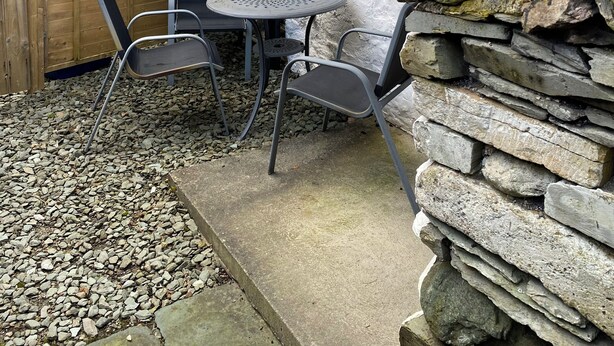 Un muro de piedra con una valla de madera, una mesa de metal con sillas, y un montón de piedras.