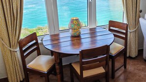 A round wooden table with four chairs, a colorful lamp, and a view of the ocean through large windows.