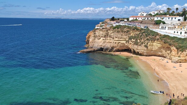 A coastal town with a beach, cliffs, and a boat on the water.