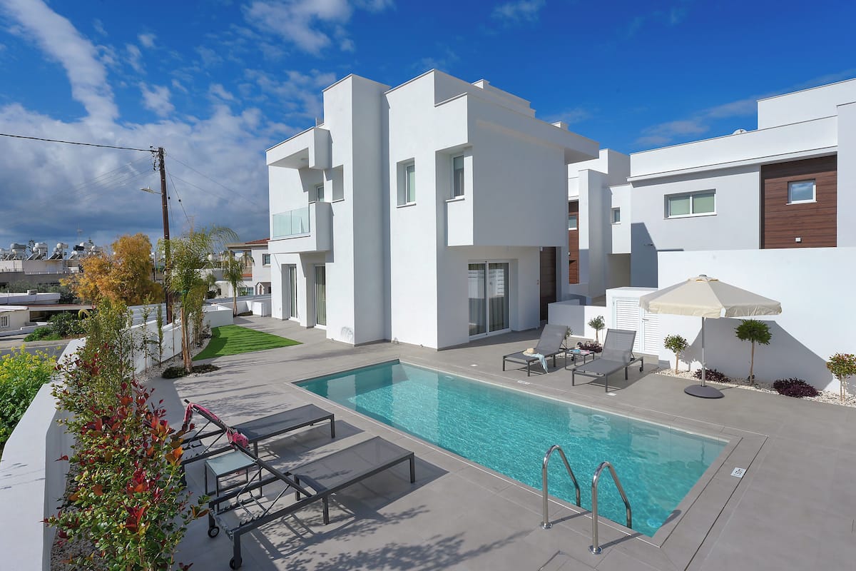 A modern pool area with a clear blue pool, lounge chairs, and a white building with a flat roof.