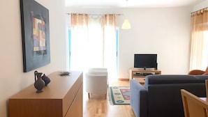 A modern living room with a sofa, TV, and a wooden cabinet. - Marina View 1 Bedroom Apartment w Swimming Pool (Albufeira)