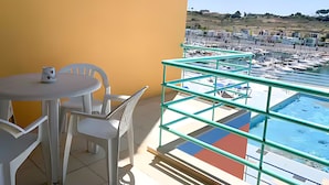 A balcony with a view of a marina and boats, white plastic chairs, and a table with a mug. - Marina View 1 Bedroom Apartment w Swimming Pool (Albufeira)