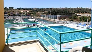 A pool area with multiple swimming pools, a marina with boats, and a view of the surrounding landscape. - Marina View 1 Bedroom Apartment w Swimming Pool (Albufeira)