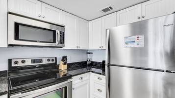 A kitchen with white cabinets, a stainless steel refrigerator, a microwave, and a stove.