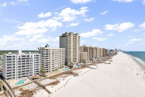 A beachfront hotel with multiple high-rise buildings, a sandy beach, and a clear sky. - Spacious beachfront condo w/  lagoon-style pool, BBQ & direct beach access! (Orange Beach)