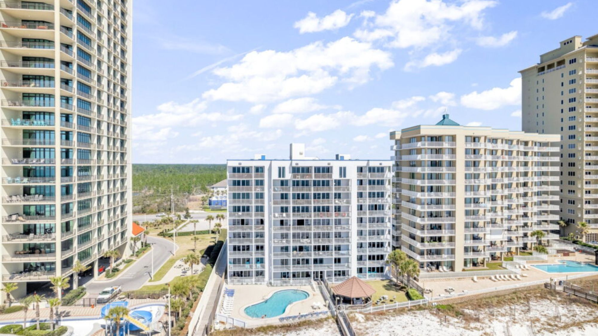 A high-rise building with multiple balconies, a swimming pool, and a beach area.