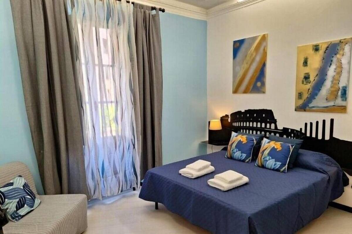 A bedroom with a bed, two pillows, a chair, and a nightstand with a lamp.