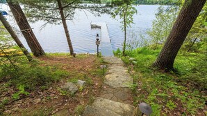 Eine Steintreppe führt zu einem Steg an einem See, umgeben von Bäumen und viel Grün.
