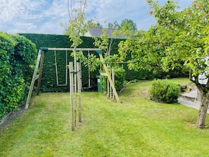 Relax in a peaceful outdoor space surrounded by lush greenery and a family-friendly wooden swing set.