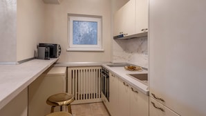 A compact kitchen with a window, built-in appliances, and a radiator.