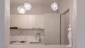 A modern kitchen with marble countertops, a gold faucet, and a white bust sculpture.