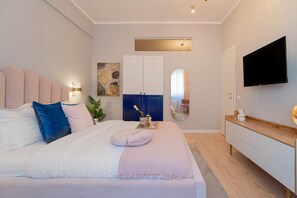 A modern bedroom with a large bed, a bedside table with a bottle and glasses, a TV mounted on the wall, and a wooden dresser. - Stunning 2BR With Balcony on Piata Universitatii (Bucharest)