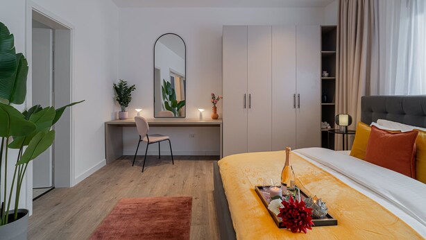 A modern bedroom with a bed, bedside table, and a desk area with a chair. - Vibrant & Spacious 3BR Condos on Amzei Square (Bucharest)