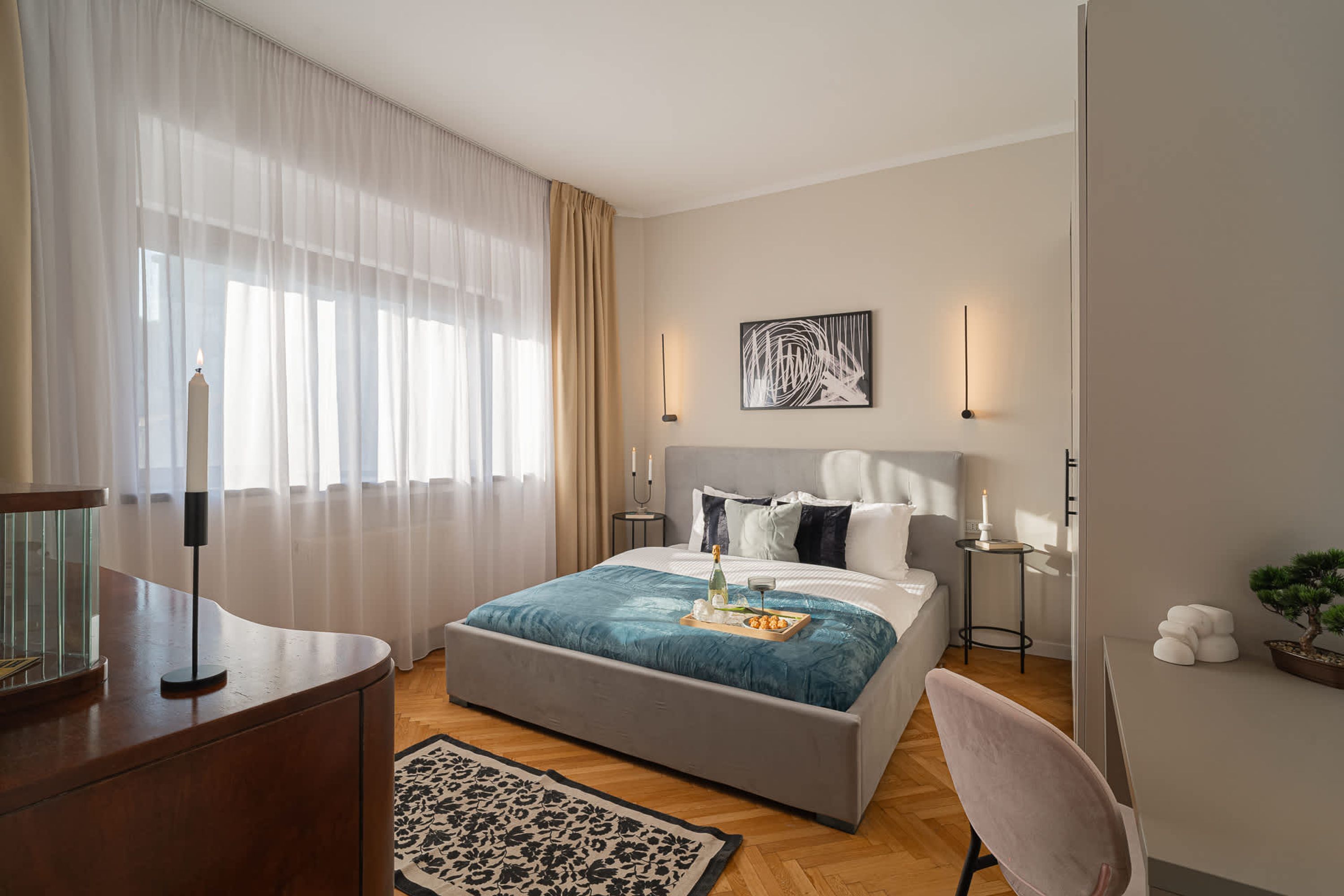 A modern hotel room with a large bed, bedside tables, a desk, and a potted plant.