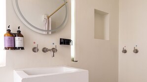 Un baño moderno con un lavabo blanco, un espejo redondo y una ducha.