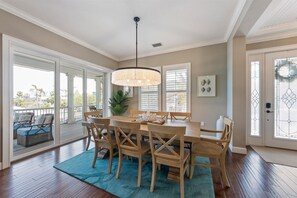 A dining area with a wooden table and chairs, a hanging light fixture, and a view through large glass doors to the outside.