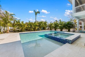 A swimming pool with clear blue water, surrounded by palm trees and a white building with a balcony.