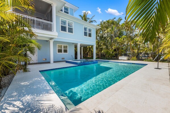 A two-story house with a swimming pool, surrounded by palm trees and a clear blue sky.