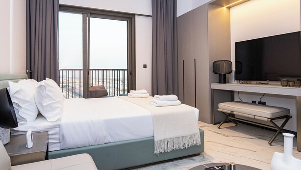 A modern hotel room with a large bed, a desk with a flat-screen TV, and a view of the outdoors.