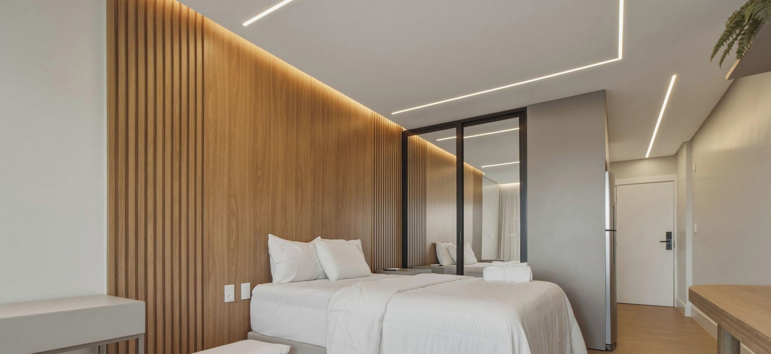A modern hotel room with a wooden accent wall, a large bed, a bedside table, and a mirror.
