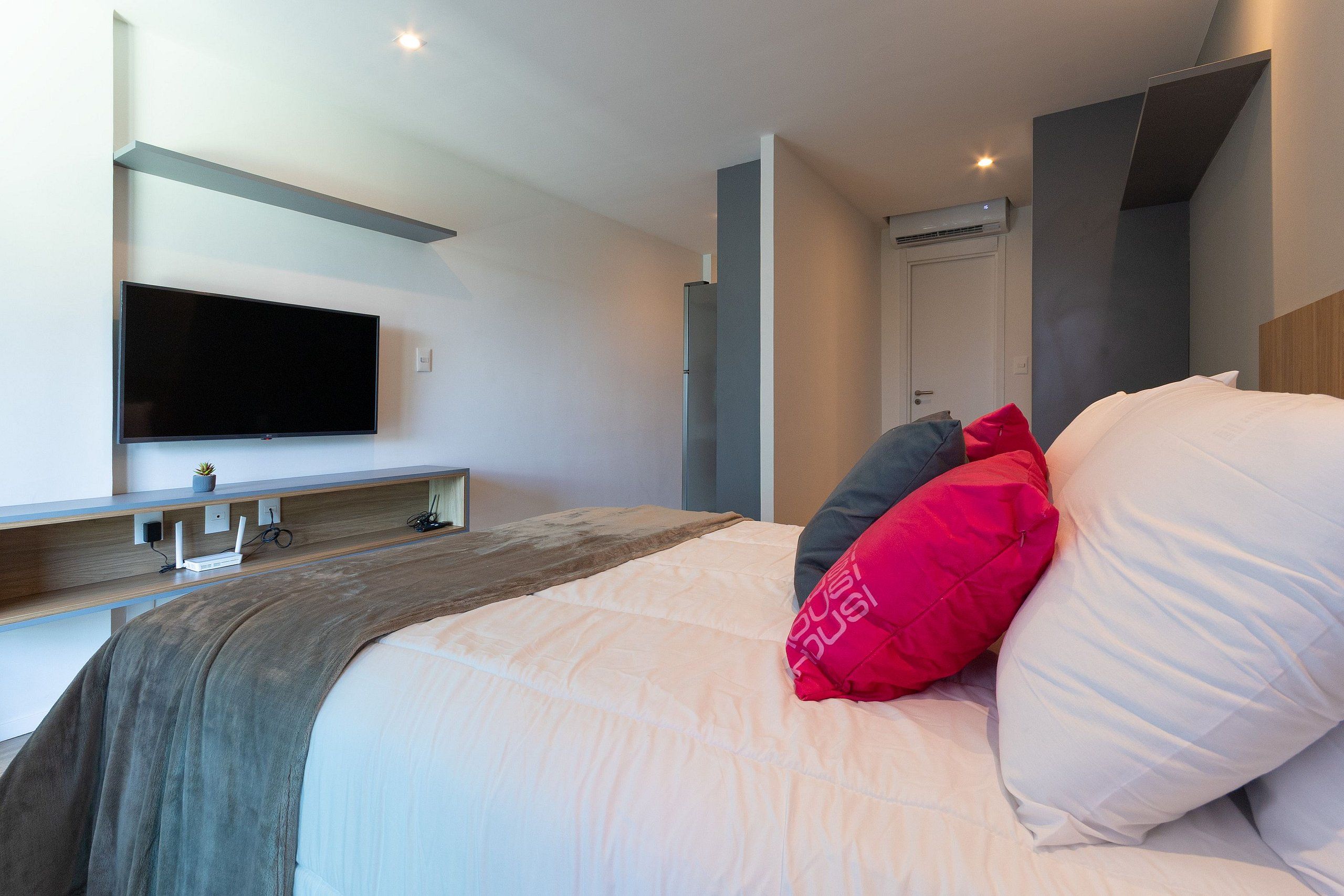Une chambre d’hôtel moderne dotée d’un grand lit, d’un téléviseur à écran plat fixé au mur et d’une table de chevet en bois agrémentée d’une plante et d’une station de recharge.