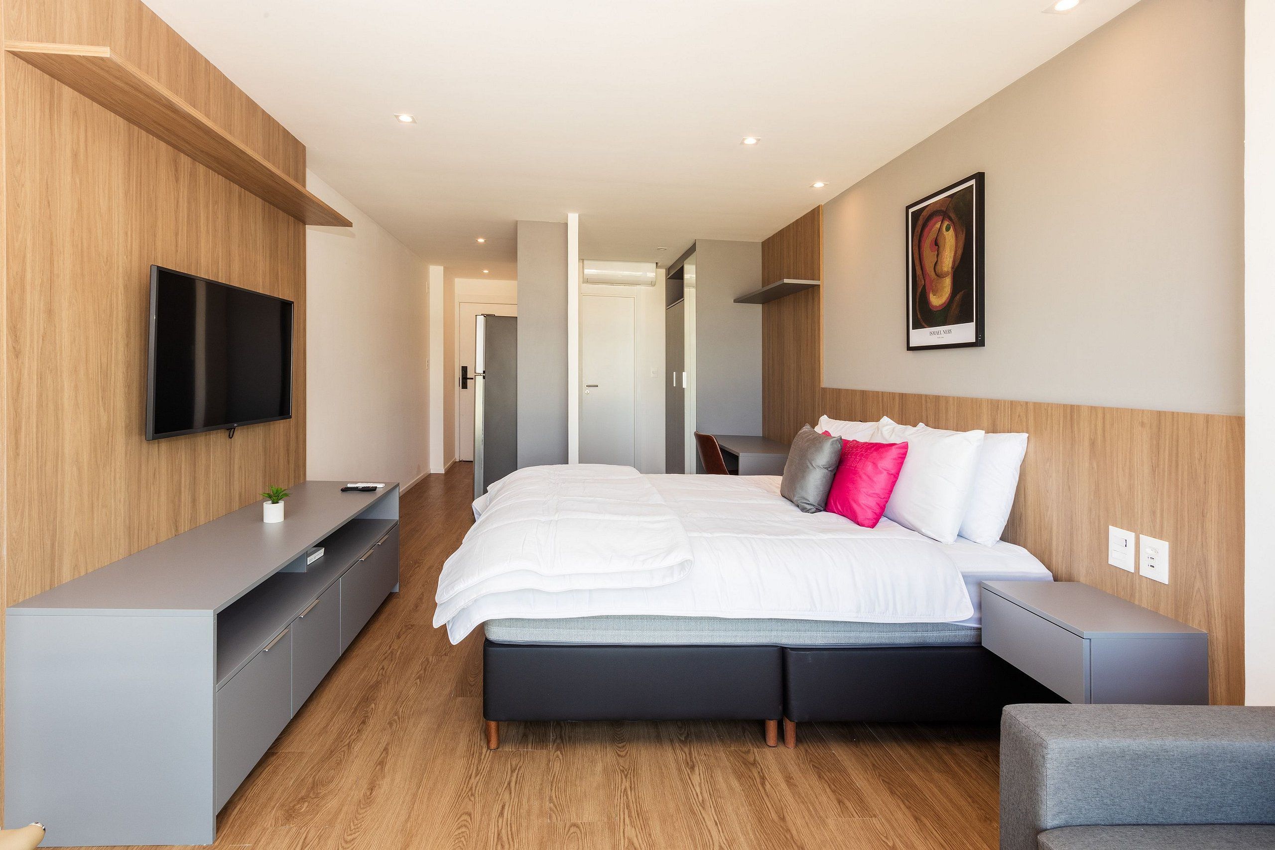 Un dormitorio moderno con cama, mesitas de noche, televisor y un cuadro en la pared.