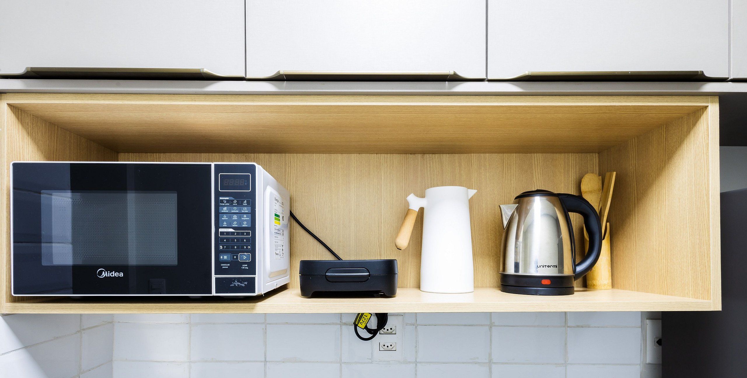 A kitchen shelf with a microwave, a white pitcher, and a coffee maker.