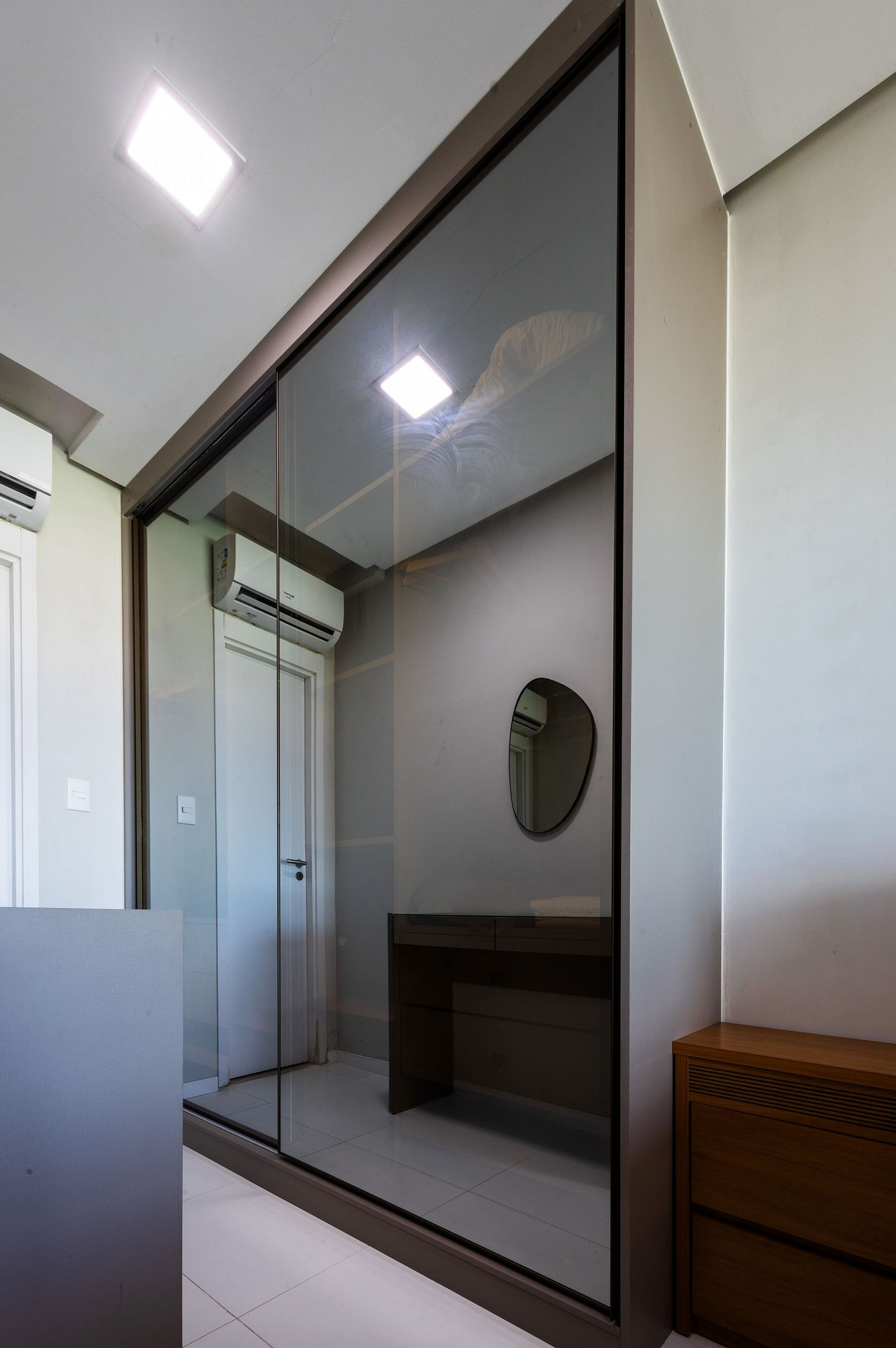 Un baño moderno con cabina de ducha de vidrio, un espejo redondo y un mueble de tocador de madera.