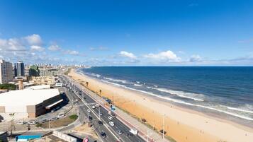 Un paisaje urbano costero con playa, una carretera con vehículos y un edificio grande con un letrero.